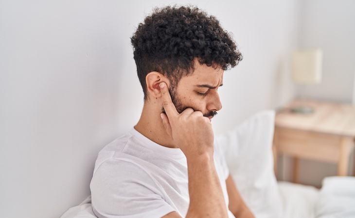 person with ear infection grabbing ear in pain while sitting on bed