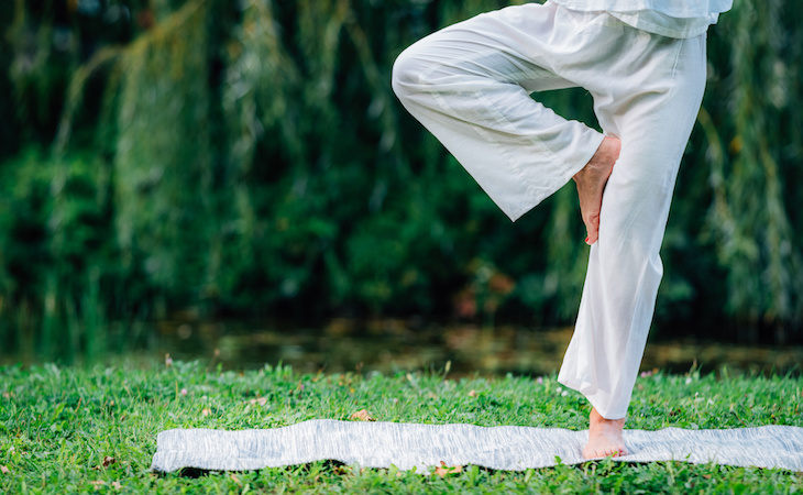 person doing yoga tree pose on grounding sheet outside