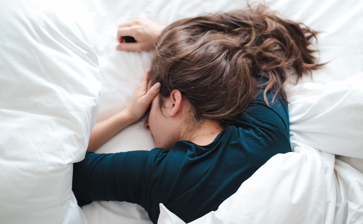 person lying in bed holding head and feeling groggy