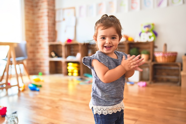 Toddler standing on the floor applauding and smiling at kindergarten
