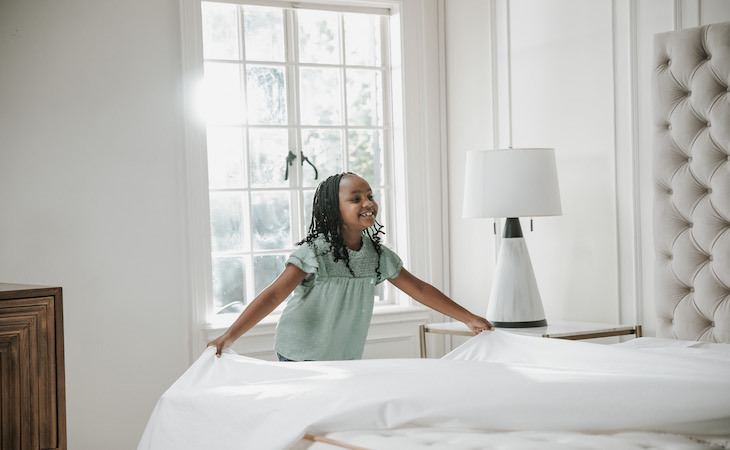 Little girl making bed in sunshine.